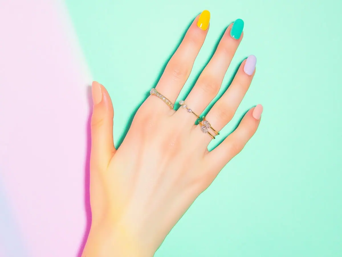 Colourful minimalist manicure featuring bright yellow, mint green, and lavender polish on almond nails, on a pastel background